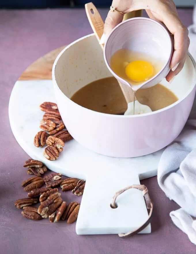 The egg being added to the butter, sugar and honey mixture in the pot