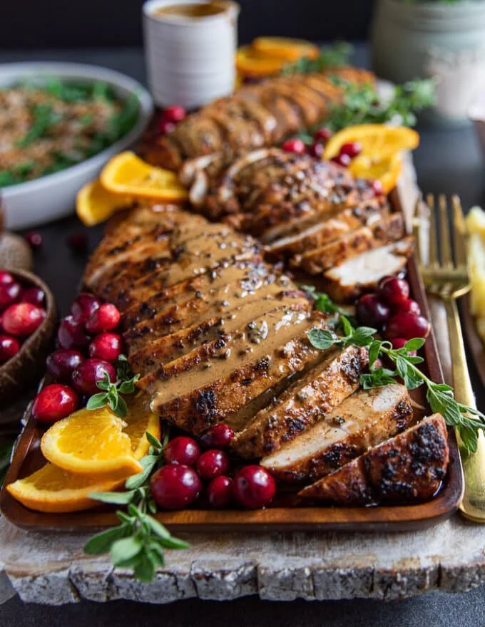 Gravy drenched turkey tenderloin recipe on a platter with orange slices and cranberries close up
