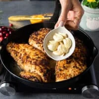 Turkey is golden and flipped and then more flavors are added like a hand holding whole garlic.