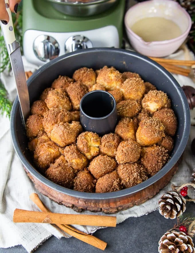 Cinnamon roll monkey bread baked and ready out of the oven. A knife is run around the pan to release the monkey bread