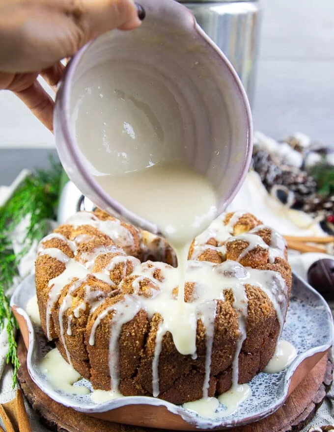 A hand pouring the cream cheese icing over the monkey bread generously