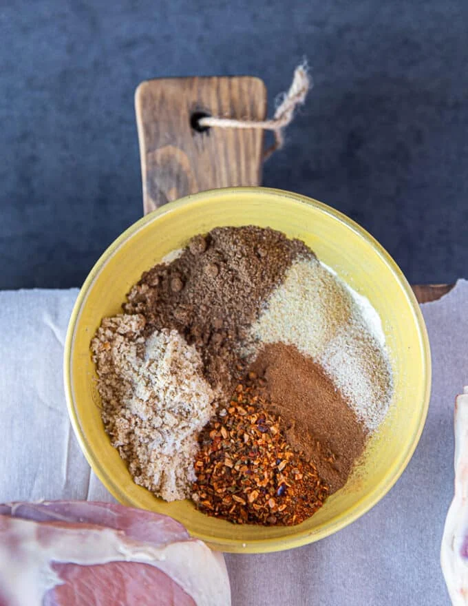 A plate with a variety of dry spice rub for the leg of lamb including salt, pepper, turkish pepper flakes, paprika, cinnamon, brown sugar, garlic powder,
