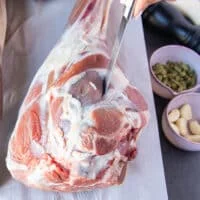 A hand using a sharp paring knife making slits along the leg of lamb