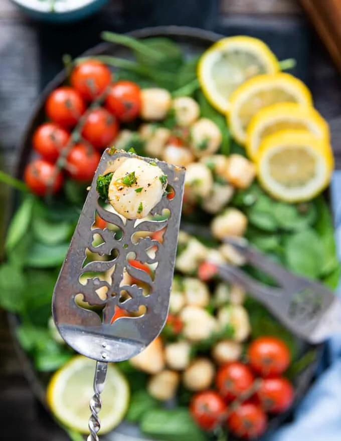 A spoon holding up one piece of scallop cooked in air fryer to show how well cooked it is