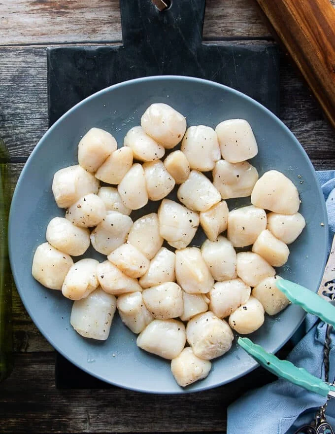 Seasoned scallops in a bowl with salt, pepper and olive oil