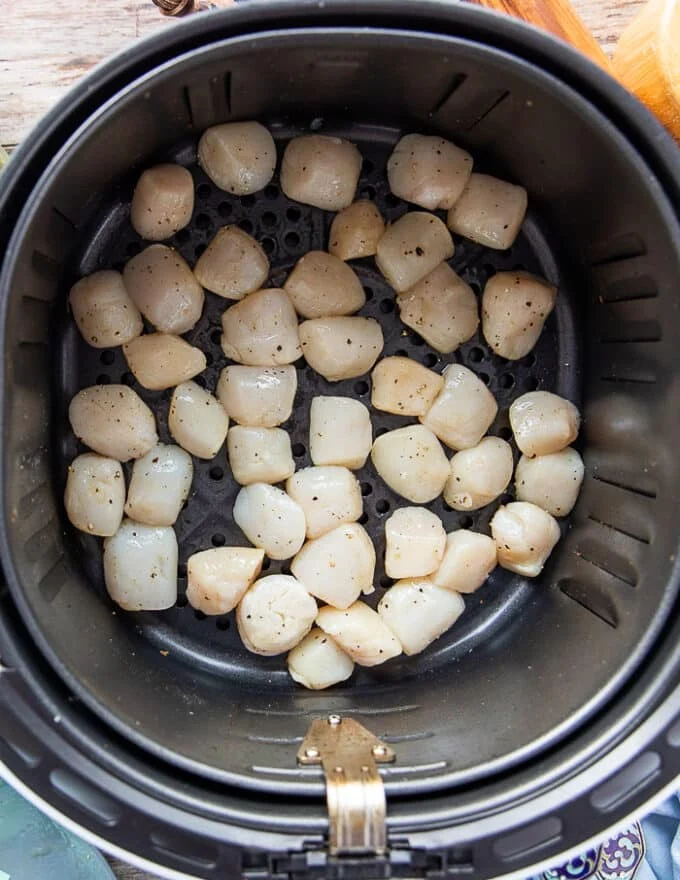 Scallops arranged in a single layer in the air fryer basket ready to cook