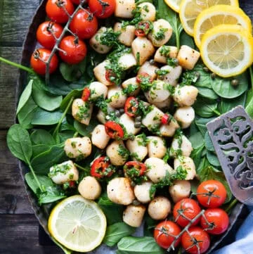 A plate of air fryer scallops over a bed of spinach, tomatoes, and drizzled with chimichurri sauce