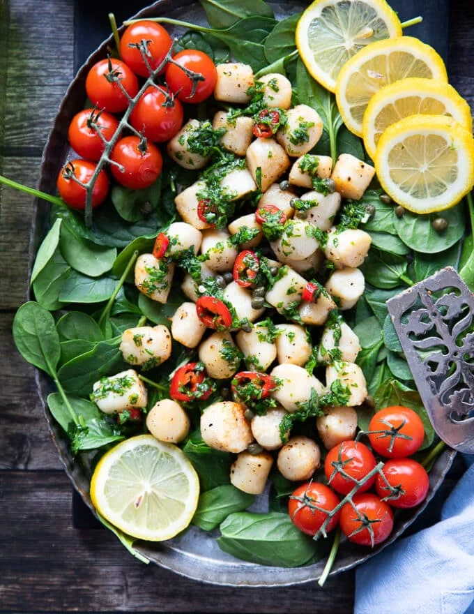 A plate of air fryer scallops over a bed of spinach, tomatoes, and drizzled with chimichurri sauce