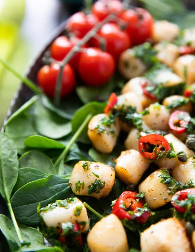 Cooked scallops in the air fryer served over a bed of spinach and drizzled with chimichurri sauce