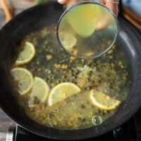 A hand pouring in some stock to finish off the chicken scallopini sauce