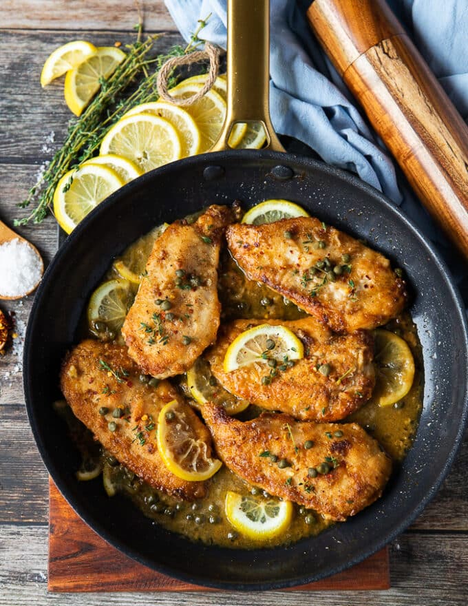 A skillet with chicken scallopini cooked up in it with lemon slices, capers and golden brown seared chicken breast