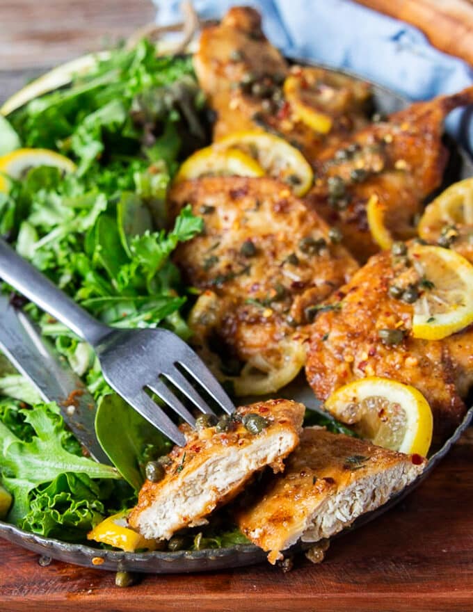 A fork holding a cut up piece of chicken scallopini showing how juicy the chicken is on the inside and how beautiful the crust is on the outside