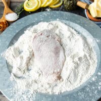 Chicken breasts placed in the shallow plate of seasoned flour and covered on both sides