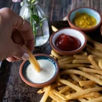 a hand dipping the french fries in a ranch dip bowl