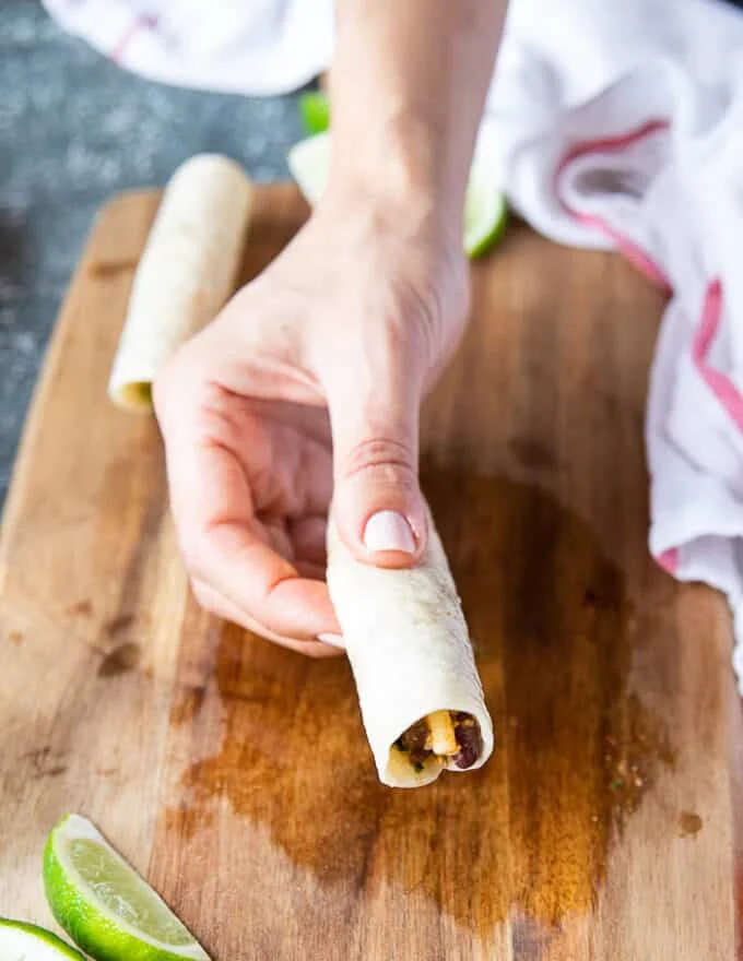 A hand holding a rolled up taquitos showing how it should look like before cooking
