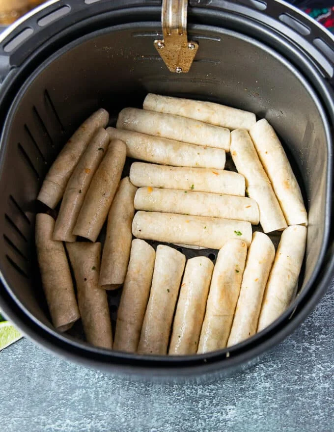 The rolled up taquitos in a single layer at the bottom of an air fryer basket.