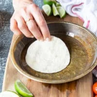 A hand dipping in the flour tortillas one by one into the plate with oil.