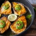 Chilean Sea bass cooked in a skillet with a gorgeous golden crust surrounded with lemon slices and topped with a dollop of basil pesto
