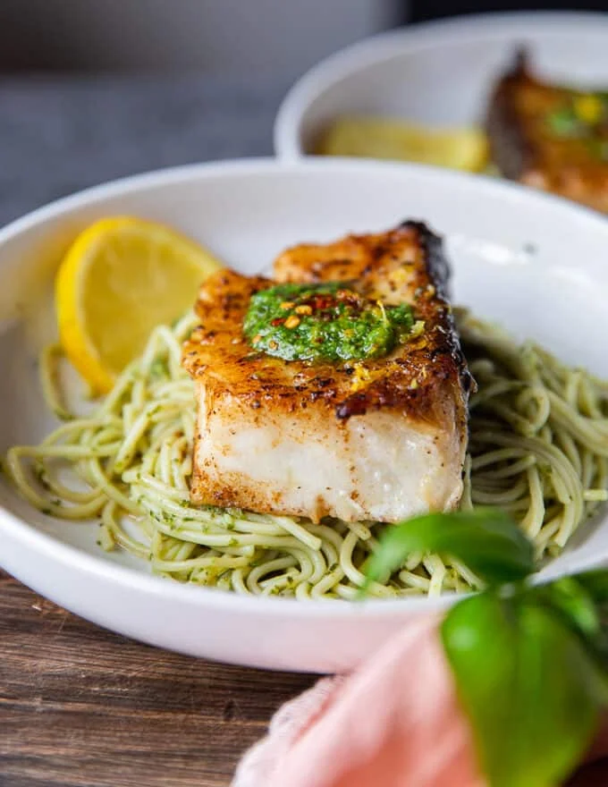 one plate of cooked chilean sea bass over a bowl of lemon pasta