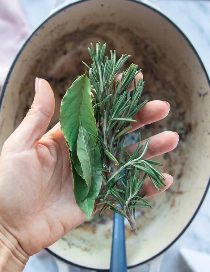 A hand holding fresh rosemary sprigs and bay leaves