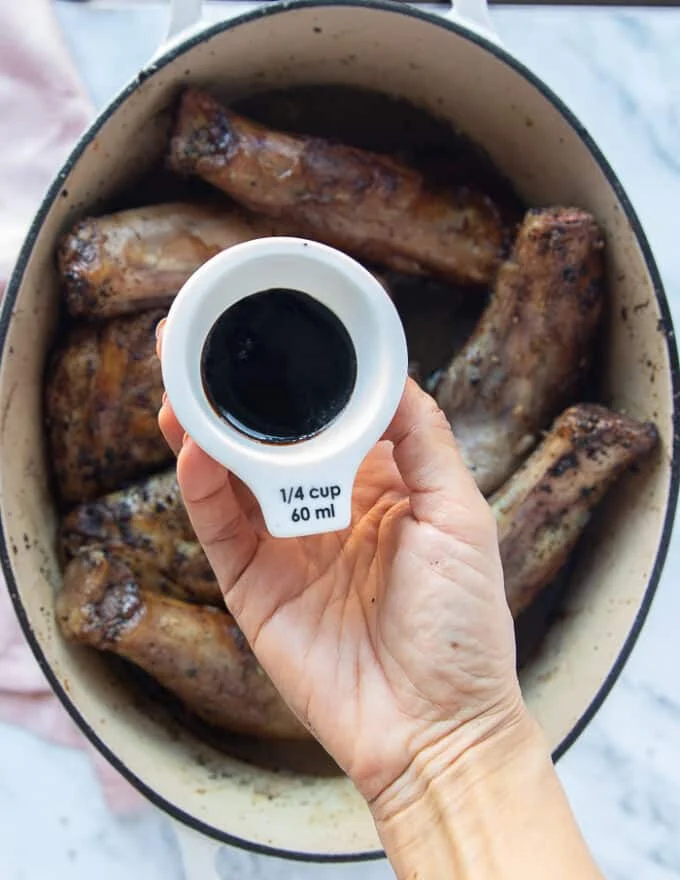 A hand holding a 1/4 cup of pomegranate molasses to add a touch of sweet and tang to the braised lamb shanks