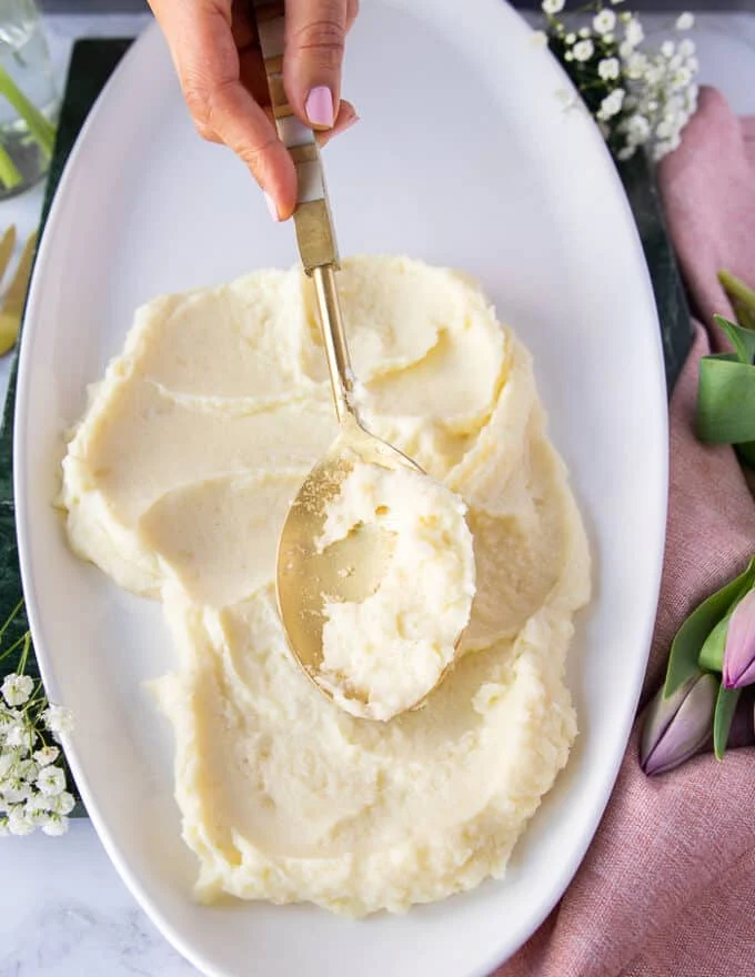 A hand spreading the mashed potatoes over a plate