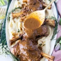A hand spooning some braising sauce over the braised lamb shanks