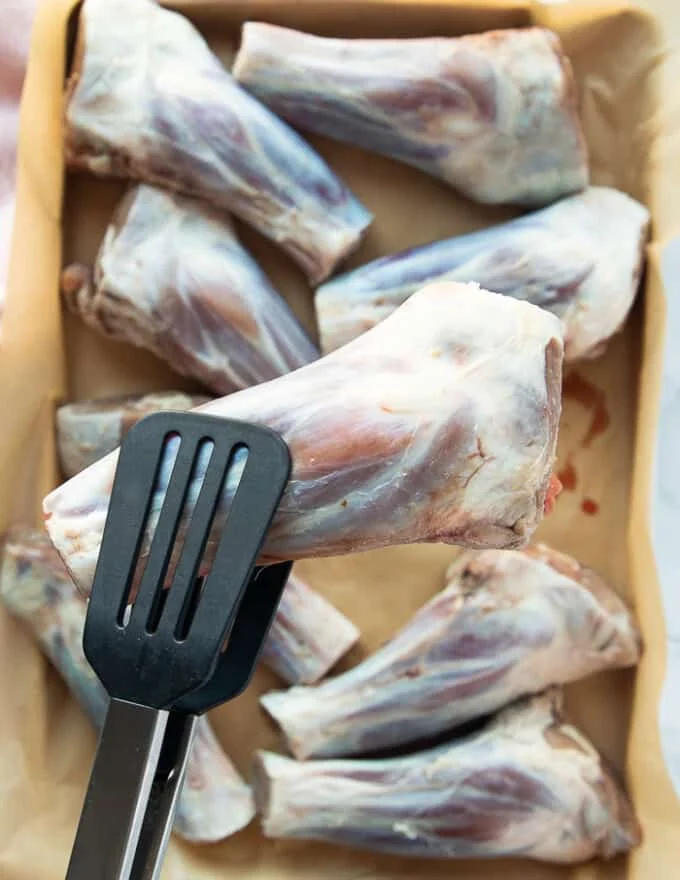 A tong holding up a piece of lamb shank to show how the lamb looks