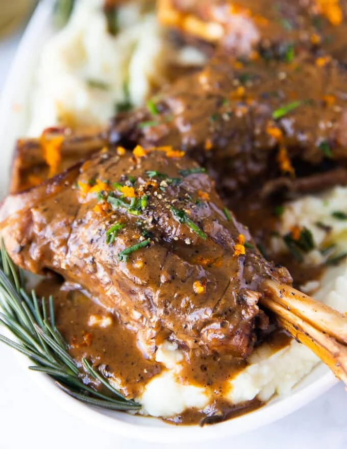 close up of one braised lamb shank served over mashed potatoes and drenched with gravy