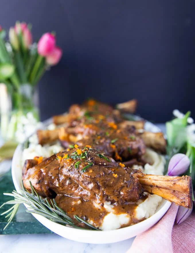 side view of the lamb shanks on a plate surrounded by fresh rosemary