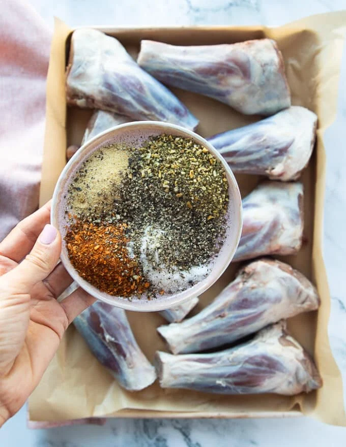 A hand holding a plate of spice blend including salt, pepper, paprika, garlic and onion flakes