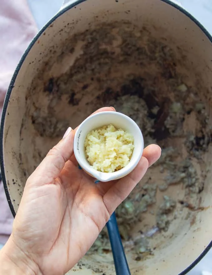 A hand adding garlic and onions to the pot to make the braising liquid