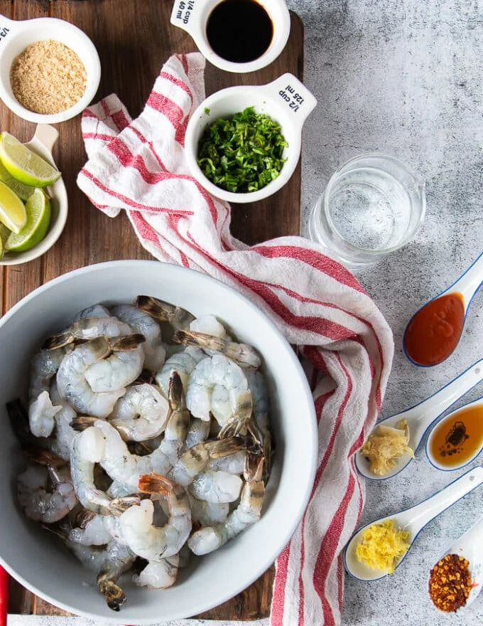 ingredients for the chili lime shrimp including raw, peeled and deveined shrimp, some lime, cilantro, chillies, soy sauce, brown sugar, sesame oil, ginger, garlic, hot sriracha sauce, lime juice, water,