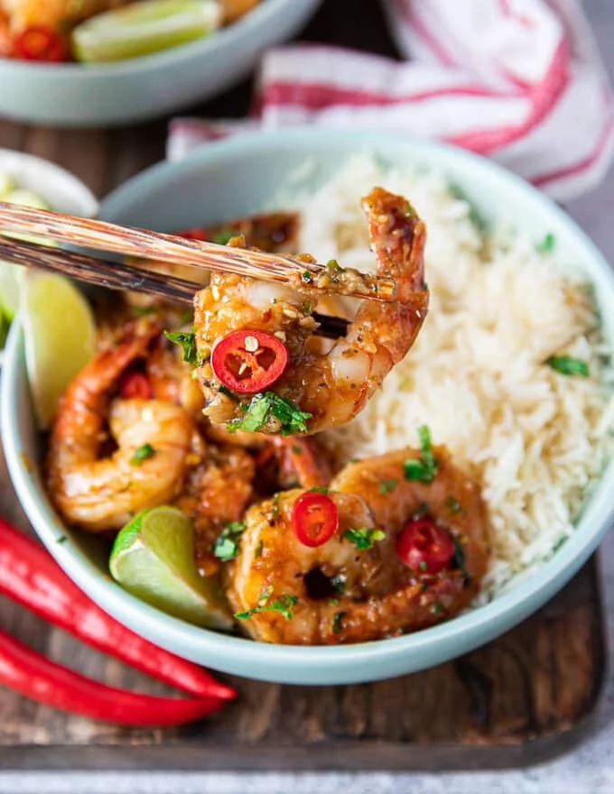 A chop stick holding a chilli lime shrimp cooked over white rice