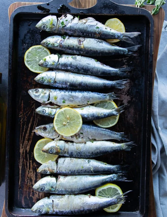 Flavored sardines on a baking sheet with lemon slices ready to go in the oven to bake
