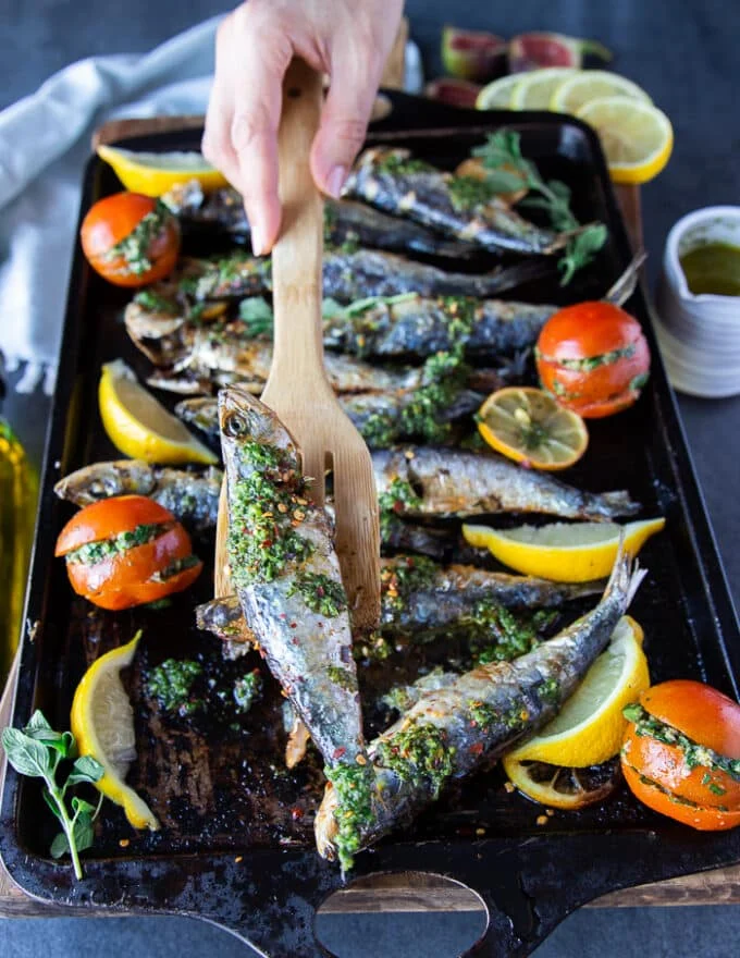 A hand holding a cooked sardine with a wooden spoon showing the perfectly cooked fish