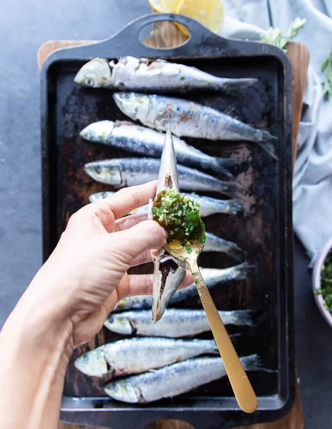 A spoon slathering the ingredients for sardine recipe inside the gut of fresh sardines to flavor it