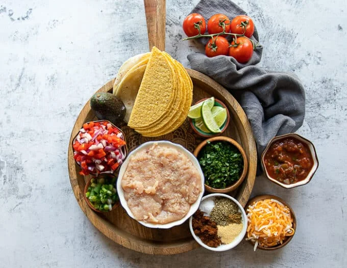 Ingredients for ground chicken tacos including ground chicken, homemade taco seasoning, fresh salsa, cilantro, lime, tomatoes, avocados, cheese, taco shells
