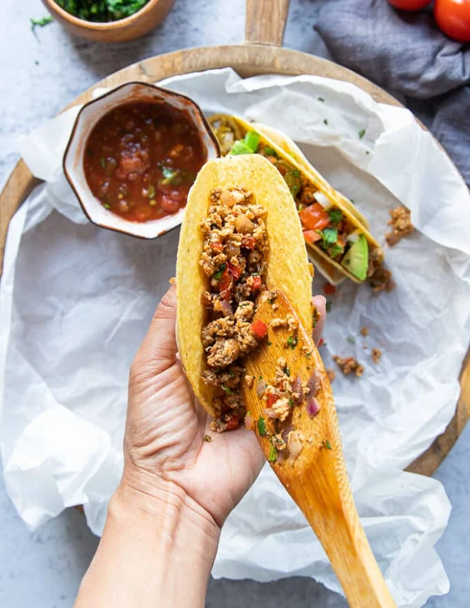 A hand loading the ready tacos with the ground chicken mixture filling up the taco shell