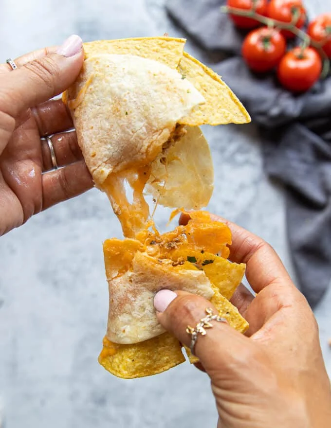 A hand stretching the ground chicken tacos breaking up the shell and showing the cheese pull
