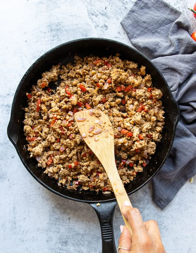 Ground chicken mixture cooking in a cast iron skillet with onions, bell peppers and spice