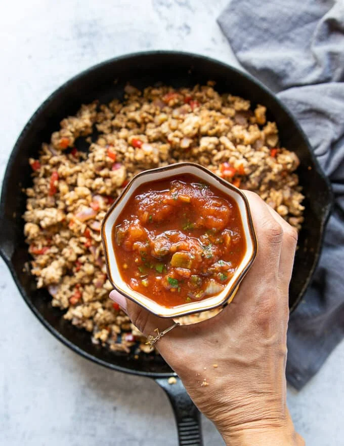 A hand holding homemade salsa to be added into the ground chicken mixture