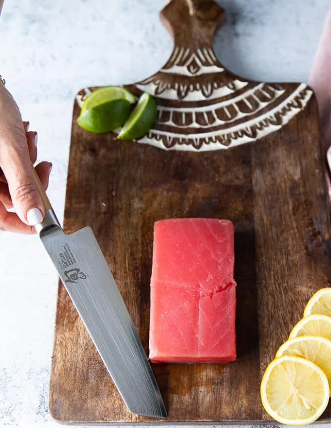A hand holding a super sharp knife ready to slice the tuna