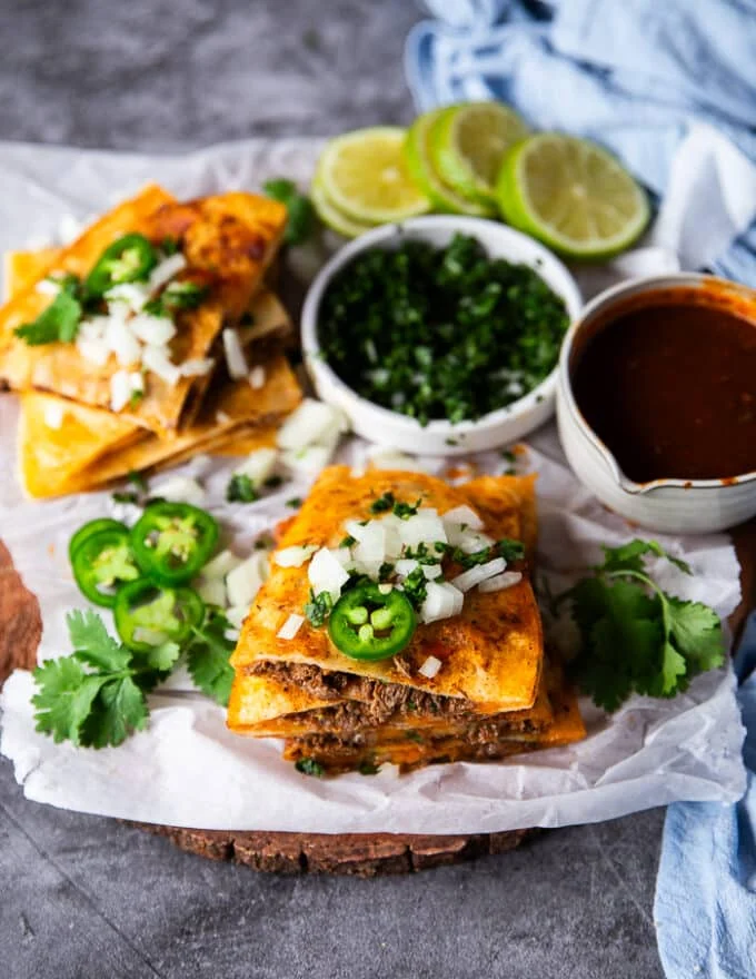 Cut up birria quessadillas golden right off the pan and topped with cilantro, chopped onions and jalapenos with a side bowl of birria stew for dipping