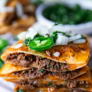 Close up of a cut open birria quesadilla showing the birria meat and cheese and onion jalapeรฑo topping
