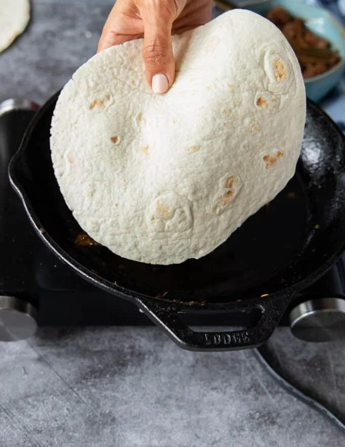 A hand holding a tortilla ready to put in a hot pan over medium heat with some oil