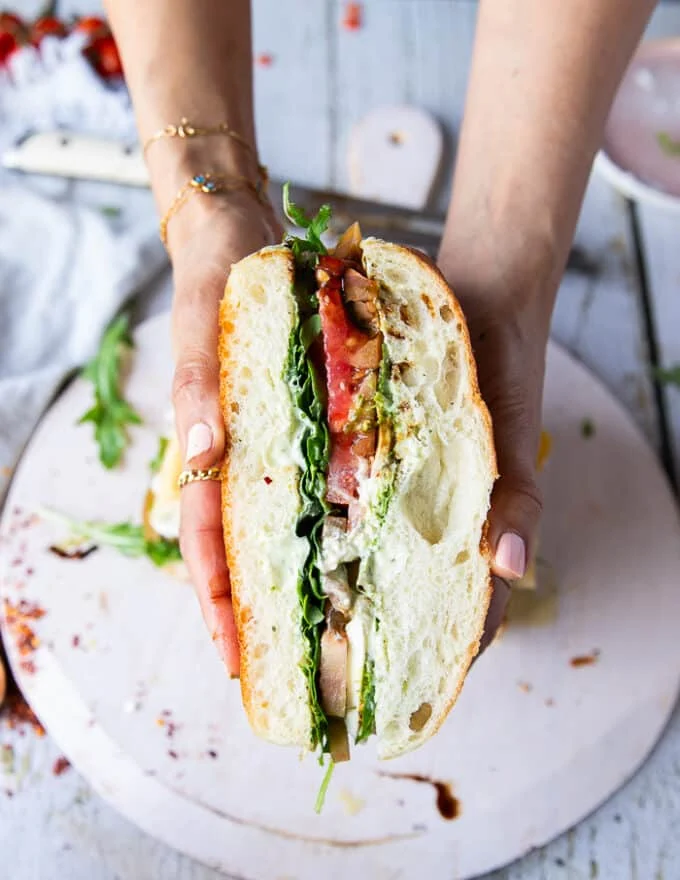 A hand holding a slice of the caprese sandwich recipe showing the beautiful layers of ingredients