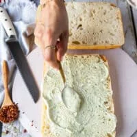 A hand spreading a layer of basil mayo over the bread to start making caprese sandwich