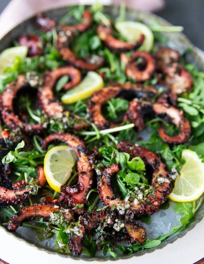 Close up of a plate of grilled octopus surrounded by lemon slices and arugula