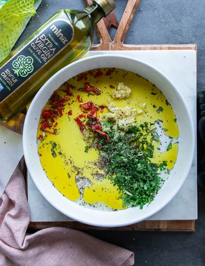 All the marinade ingredients added on to a shallow plate including olive oil, lemon juice, garlic, fresh herbs, seasoning